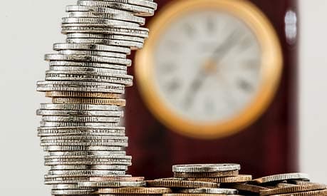 a pile of silver coins in the foreground and a clock in the background
