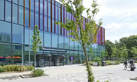 Alliance Manchester Business School in the sunshine with green trees at the front